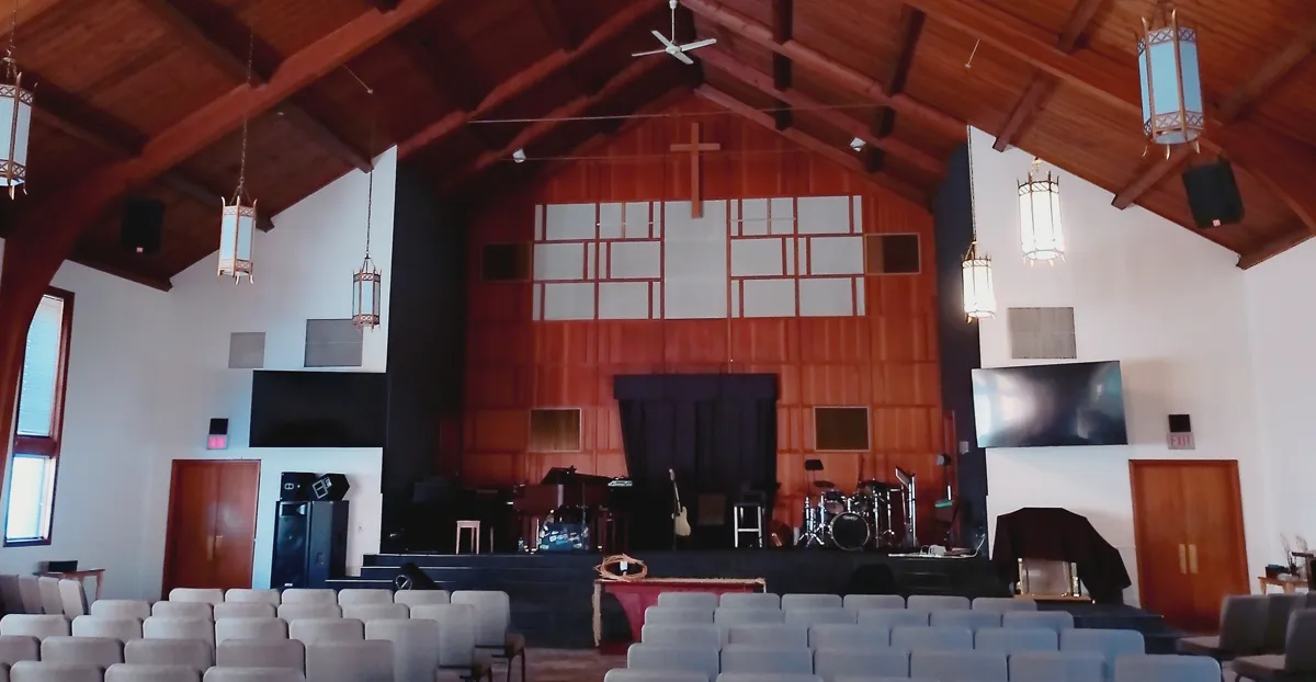 The sanctuary at St Johns Church with wood beams, a cross and rows of chairs